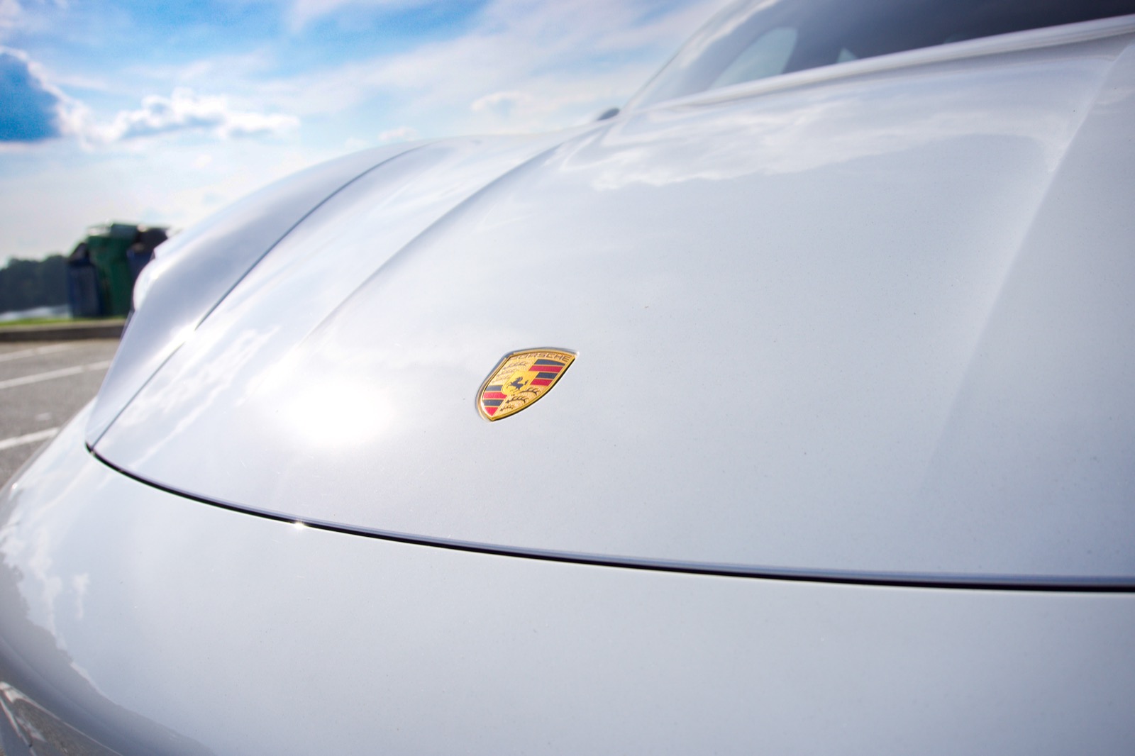 Porsche crest on the hood of a white sports car under a bright sky.